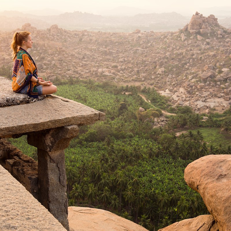 Young Woman Meditating Over Ancient City Landscape At Sunrise In Hampi, India.  Copy Space