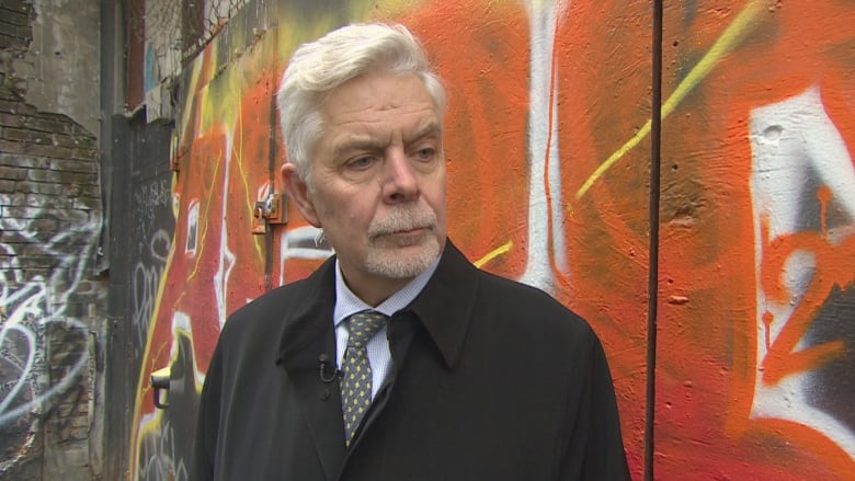 Headshot Photo Of Vancouver Psychiatrist Dr Bill Macewan Standing In Front Of An Orange Colored Wall With Graffiti On It. 