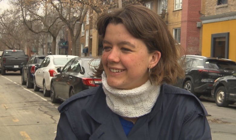 A Woman With Short Hair And A Neck Warmer On A Bike Path Smiles At The Camera. 