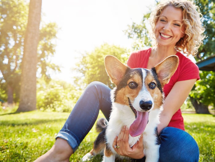 A smiling person is playing with a dog outdoors.
