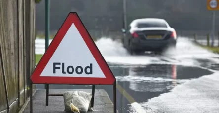 MotoristDrivingThroughFloodWatersWithWarningSignInForeground